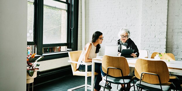 Two women sitting at a table looking at a laptop