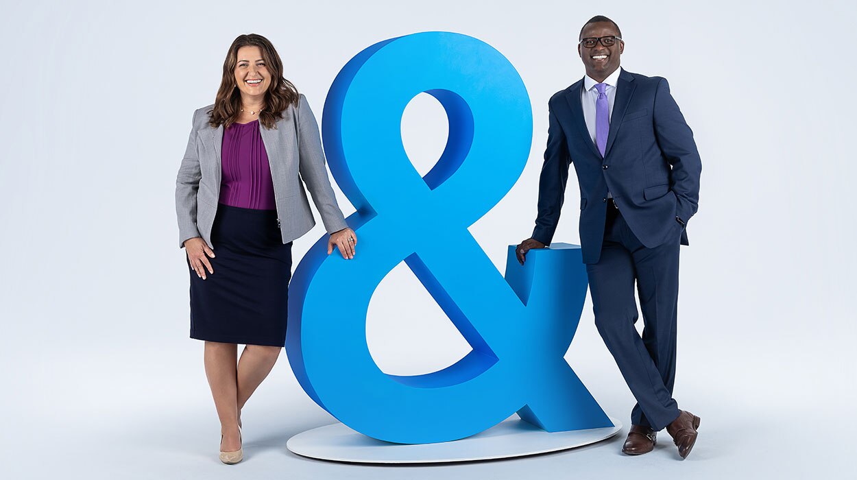 Two people leaning against a three-dimensional, life-sized ampersand.